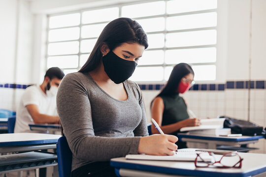 Brazilian college students wearing face masks sitting at the desk in the classroom. Concept of reopening of educational institutions in the COVID-19 pandemic