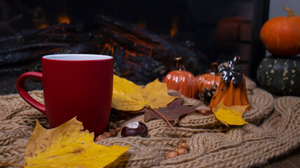 Red mug with tea on the background of a soft, knitted scarf, autumn leaves, pumpkin. Autumn background, cozy evening, fireplace.
