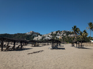 Camastros en playa de Acapulco. Al fondo cerro con viviendas.