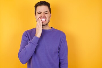 Handsome man with sweatshirt over isolated yellow background touching mouth with hand with painful expression because of toothache or dental illness on teeth.
