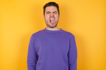 Handsome man with sweatshirt over isolated yellow background sticking tongue out happy with funny expression. Emotion concept.