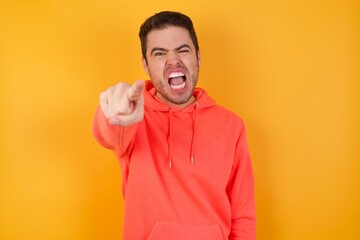 Handsome man with sweatshirt over isolated yellow background pointing displeased and frustrated to...