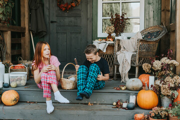children a boy and a girl in pajamas sharing candy and having fun on the porch of the backyard decorated with pumpkins in autumn