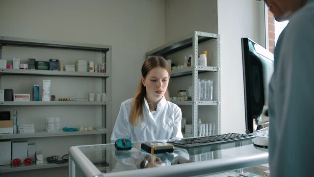 Woman pharmacist preparing medicine stuff for buyer with credit card payment. Adult caucasian male purchasing pills, cough powder in modern drug store. Professional employee seller.
