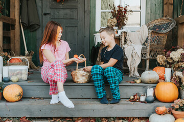 children a boy and a girl in pajamas sharing candy and having fun on the porch of the backyard decorated with pumpkins in autumn