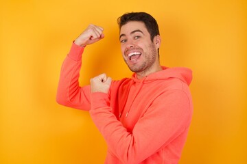 Profile photo of excited beautiful caucasian businessman wears red shirt isolated over yellow background raising fists celebrating black friday shopping
