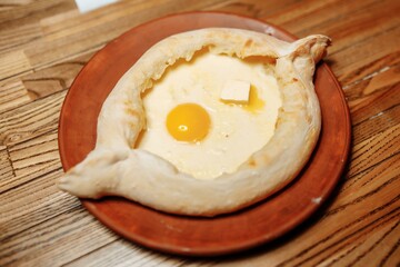 Top view on traditional Adjarian Khachapuri - open baked pie with melted salt cheese suluguni and egg yolk on wooden tray. Traditional georgian food