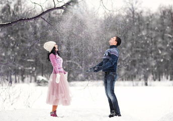 Outdoors romantic portrait of happy attractive couple in love. They throwing snow in the air. Smiling and enjoying snowy weather. Wearing knitted hat, mittens and sweaters. Love concept. Valentine day