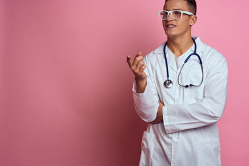 male doctor in a medical gown with a stethoscope around his neck on a pink background and glasses on his face