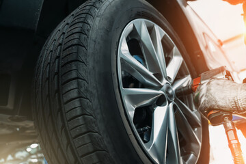 Mechanic hands with pneumatic wrench tool changes tyre or wheel of car in auto service.