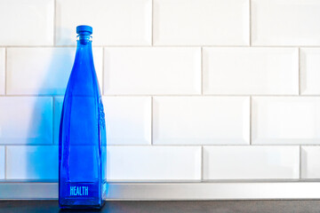 Blue glass bottle for water and other drinks with the text health on the white tile background