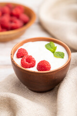 Yogurt with raspberry in clay cups on white wooden background. Side view, selective focus.