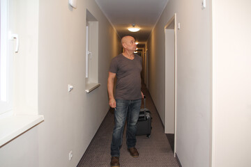 adult man walks down the hotel corridor to his room with a suitcase and keys in his hand, the concept of a long-awaited vacation, business trip