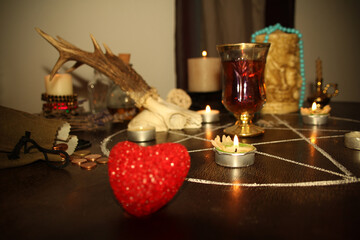 Obraz premium in a dark room candles are burning on a round esoteric table, animal skulls are lying, a pentagram is drawn, a model of a red heart, candles, a concept of magic, witchcraft