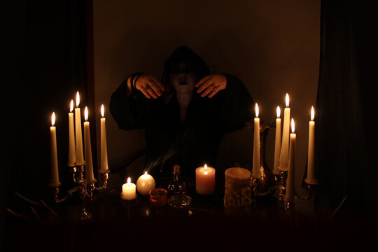 Female Fortuneteller conjures in a dark room, candles are burning on a round esoteric table with a pentagram, animal skulls lie, the concept of magic, witchcraft