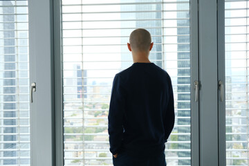 young man stands in an office in front of a window, looks at a modern European city, the concept of a business idea, a workplace