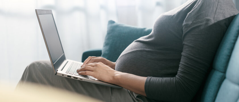 Pregnant woman sitting on the sofa and connecting with her laptop