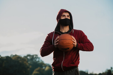 A young man with a face mask holding a basketball.