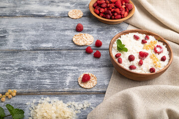 Rice flakes porridge with milk and strawberry in wooden bowl on gray wooden background. Side view, copy space.