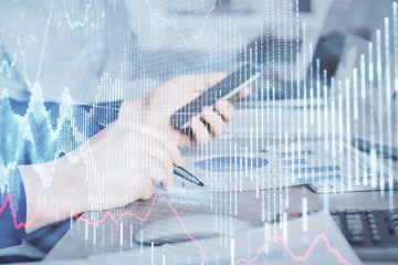 Double exposure of man's hands holding and using a digital device and forex graph drawing. Financial market concept.