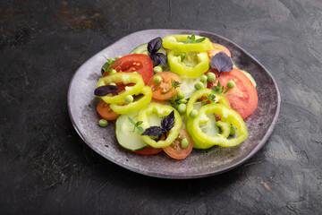 Vegetarian salad from green pea, tomatoes, pepper and basil on a black concrete background. Side view.