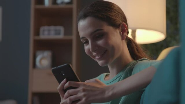 Happy woman relaxing at home and chatting with her phone