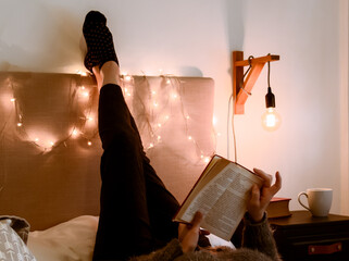 Fototapeta Pasando una tarde de otoño leyendo y descansando. Mujer adulta leyendo un viejo libro cómodamente acostada en una cálida y confortable habitación iluminada tenuemente obraz