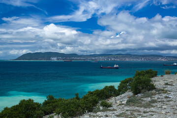 Blue sea with cargo ships against the blue cloudy sky, in the background of the city. View from the cliff