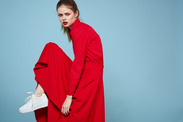 A woman in a red dress and sneakers lifted her leg up against a blue background