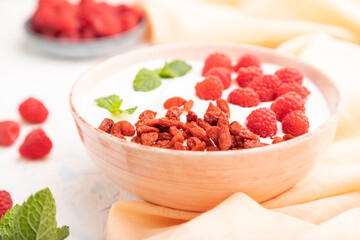 Yogurt with raspberry and goji berries in ceramic bowl on white concrete background. Side view, selective focus.