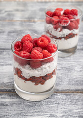 Yogurt with raspberry, goji berries and chia seeds in glass on gray wooden background. Side view, selective focus.