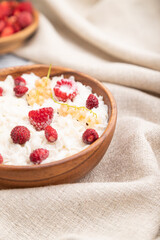 Rice flakes porridge with milk and strawberry in wooden bowl on gray wooden background. Side view, selective focus.