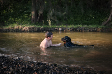 Young boy and his pet rottweiler dog sitting together in stream sharing a special moment