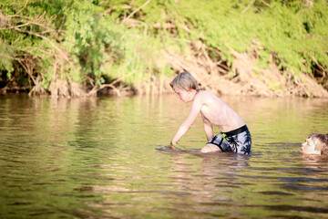Boy swimming in fresh water river at dusk in New South Wales, Australia