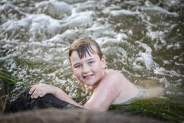 Obraz premium Boy swimming in river at dusk holding onto edge looking up at camera. Moody image with rich tones