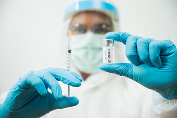 Doctor in ppe suit uniform wearing face mask protection virus holding medicine liquid vaccine vial bottle and syringe. COVID-19 concept.