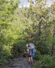 Fototapeta premium Woman hiking with baby in pack trying to figure out a way down