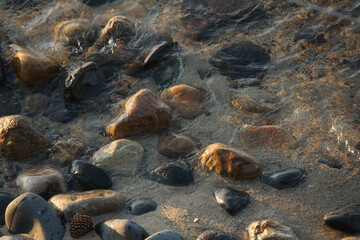 Rocks and pebbles sitting underwater on a sandy beach, during golden hour