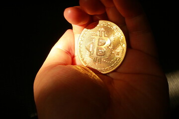 暗闇の中で黄金色に輝くビットコインを掴む手
