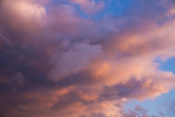 This beautiful image shows fluffy clouds glowing in shades of pink and orange clouds as they move through a blue early sunset sky.