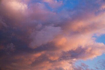 This beautiful image shows fluffy clouds glowing in shades of pink and orange clouds as they move through a blue early sunset sky.