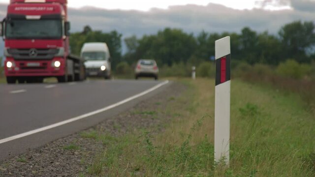cars and a truck driving past the camera, a road sign in the foreground, a roadside shot. Transport outside the city, countryside