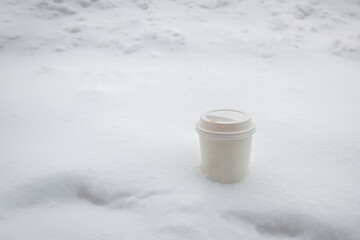 Paper cup of  hot cafe latte coffee with plastic lid covered put in the snow in the snowy day of winter.