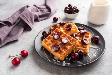 Belgian fluted waffles with fresh cherries and cream on a plate. Soft homemade waffles, sweet dessert with cherries.