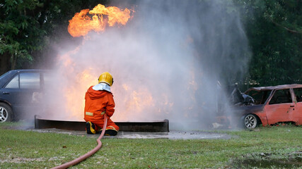 Obraz premium Firefighter fighting with flame using fire hose chemical water foam spray engine. Fireman wear hard hat, body safe suit uniform for protection. Rescue training in fire fighting extinguisher