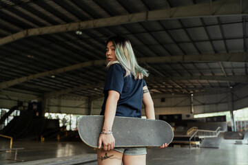 Back view - Skateboard player woman indoors court.