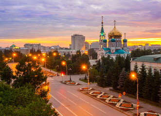 Assumption Cathedral in Omsk at beautiful orange-pink sunset. Holy Assumption Cathedral and Lenin Street