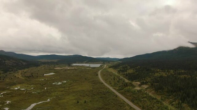 View of Scenic Road alongside Peaceful Lake surrounded by Mountains in Canadian Nature. Aerial Drone Shot. Taken near Stewart-Cassiar Highway, Northern British Columbia, Canada.