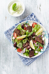 Tasty Salad with Grilled Beef Pieces, Cherry Tomatoes, feta Cheese and Kalamata Olives. Bright wooden background. Top view.	