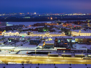 Gagarina street, Lenin street with historic buildings with green roofs, domes and clocks in Omsk on a winter evening.